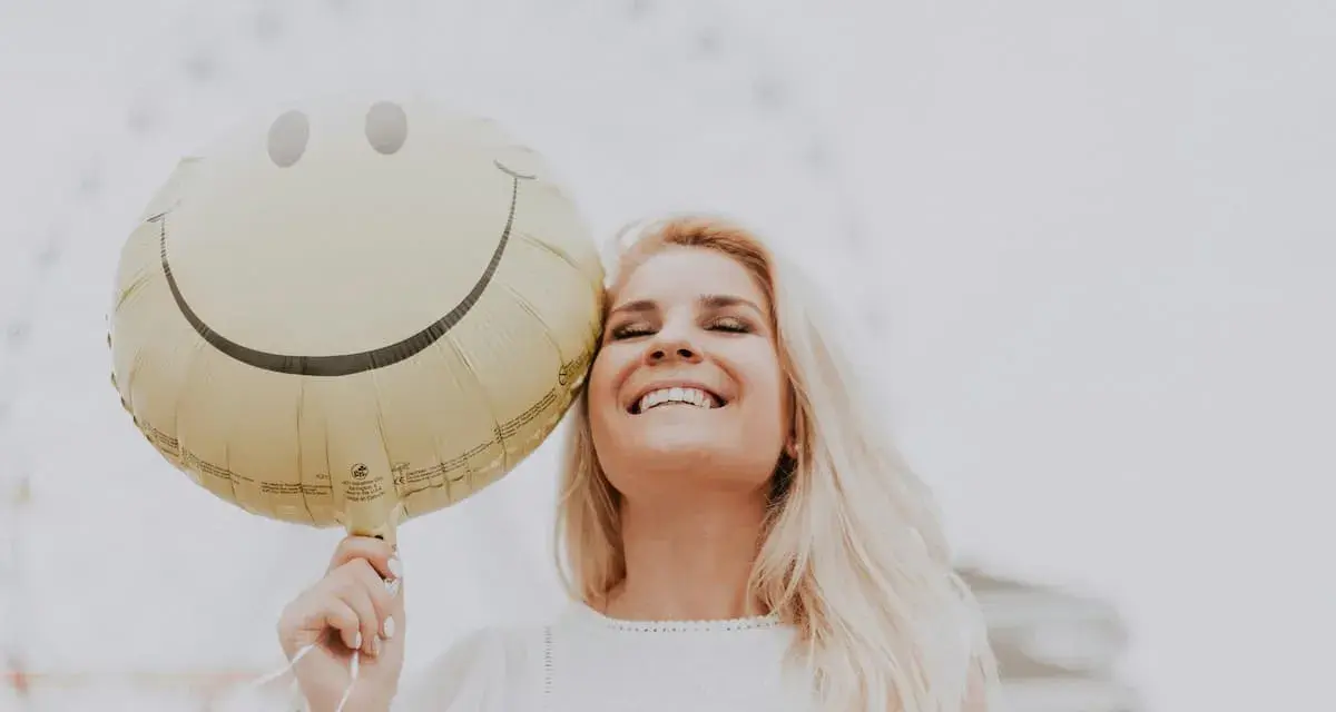 Uśmiechnięta blondynka trzymająca balon z buźką, jakby usłyszała świetny żart po angielsku.