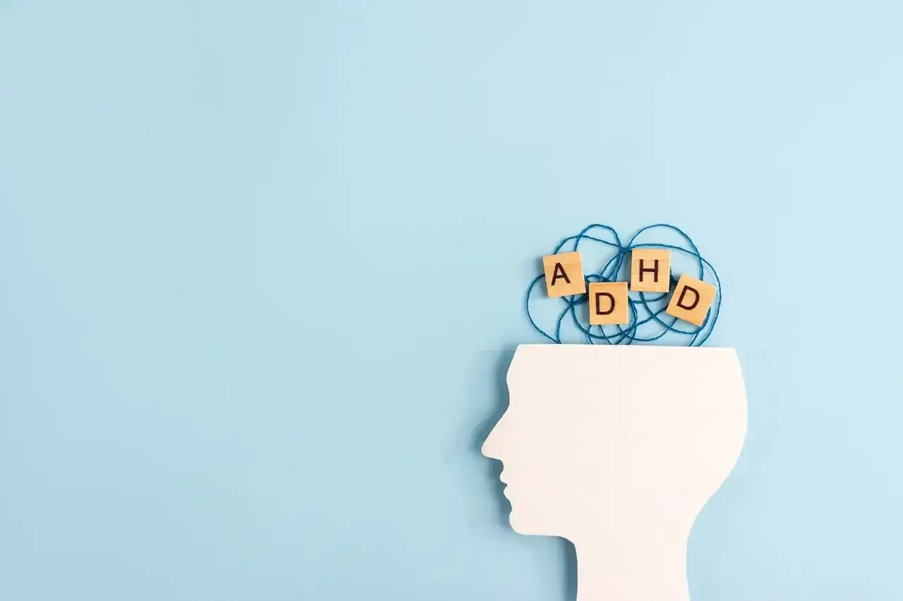 Klocki z literami ADHD wplątane w kłębek sznurka wewnątrz białego profilu głowy. Jak postępować z dzieckiem z ADHD.